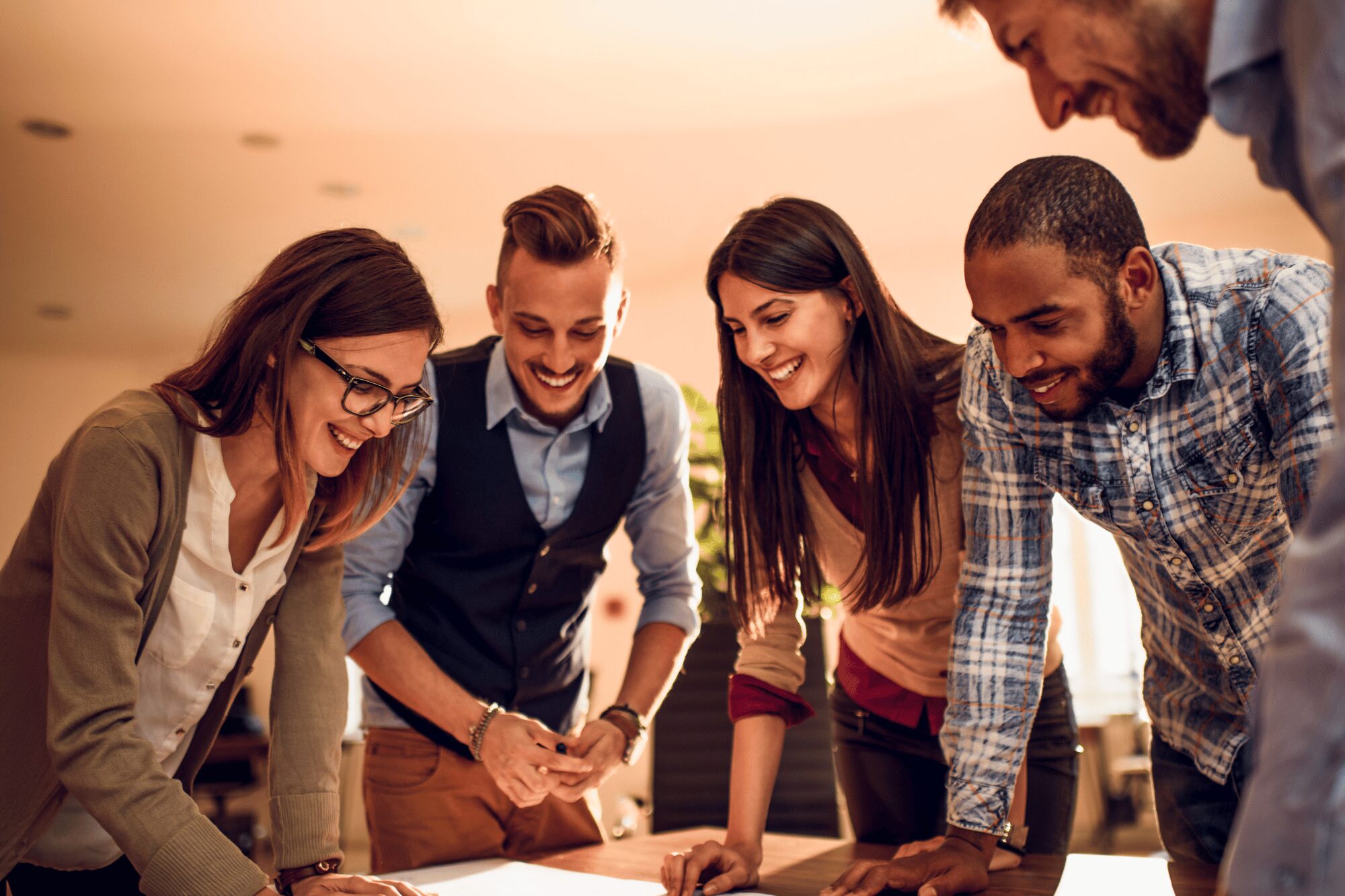 5 Kollegen stehen zusammen an einem Tisch und brainstormen