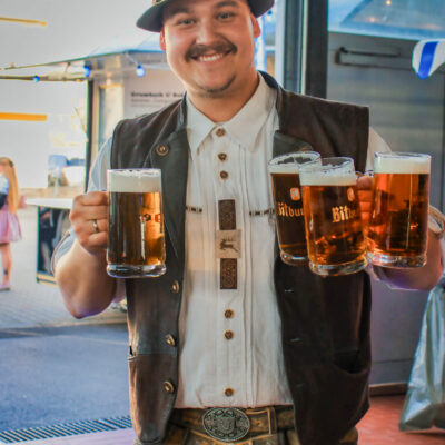 Mann in Tracht steht lächelnd mit mehreren Bierkrügen vor der Kamera