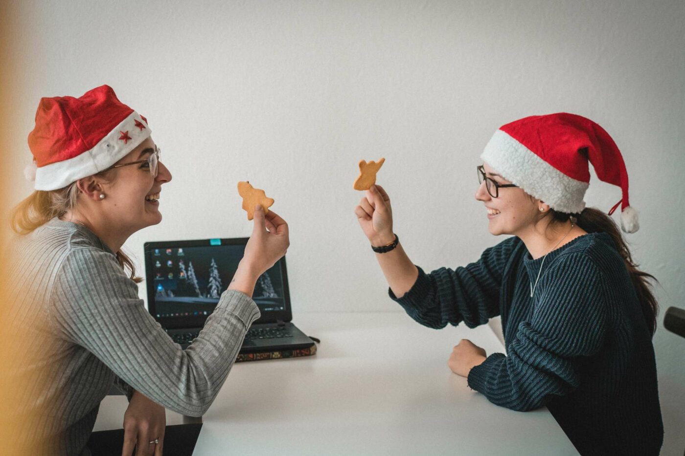 Zwei Kolleginnen sitzen mit Weihnachtsmütze am Tisch und essen Plätzchen.