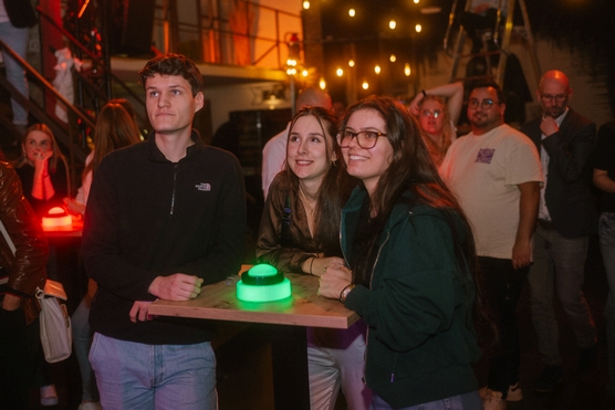 Drei Personen an einem Stehtisch mit einem grün leuchtenden Buzzer