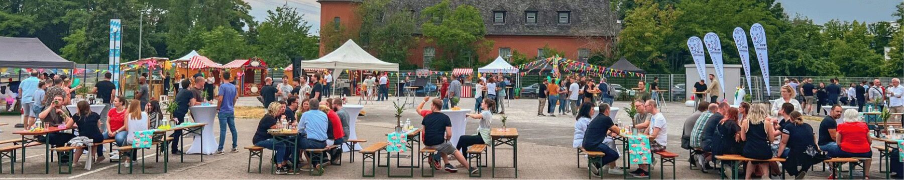 Firmenfeier Koblenz Event-Set-up: Menschen sitzen auf Bierbänken & unterhalten sich.