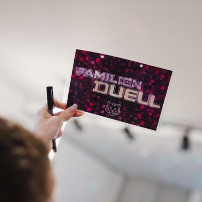 Frau hält Familienduell Karte in die Luft bei Quizshow