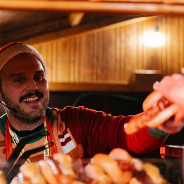 Mann mit Weihnachtsmütze serviert lächelnd einen Hotdog.