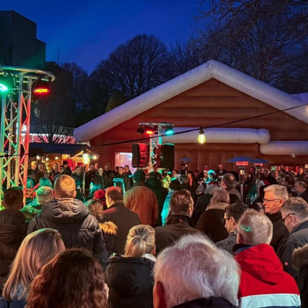 viele Menschen auf einem Weihnachtsmarkt, im Hintergrund ein winterliches Hausdach.