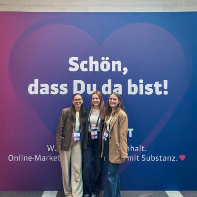 Drei Frauen stehen vor einer Fotowand bei OMT-Summit